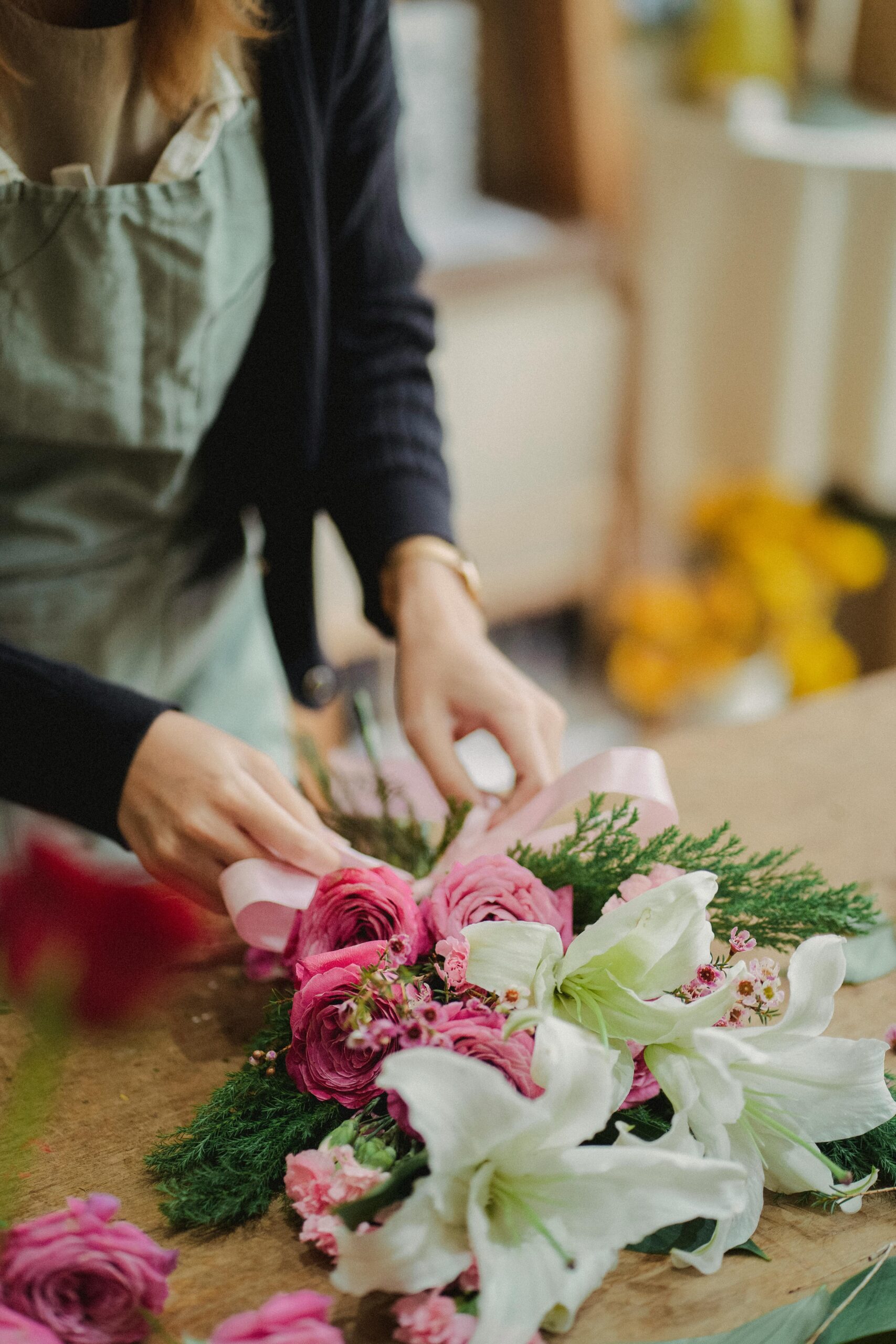 A female florist skillfully arranges a beautiful pink and white flower bouquet indoors.